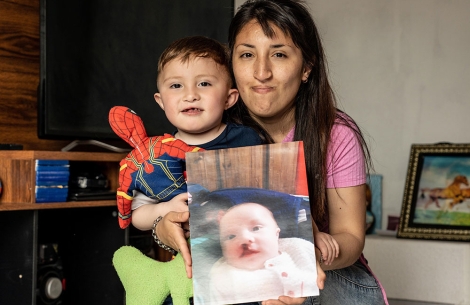 Edden, smiling, holding a picture of himself before cleft surgery