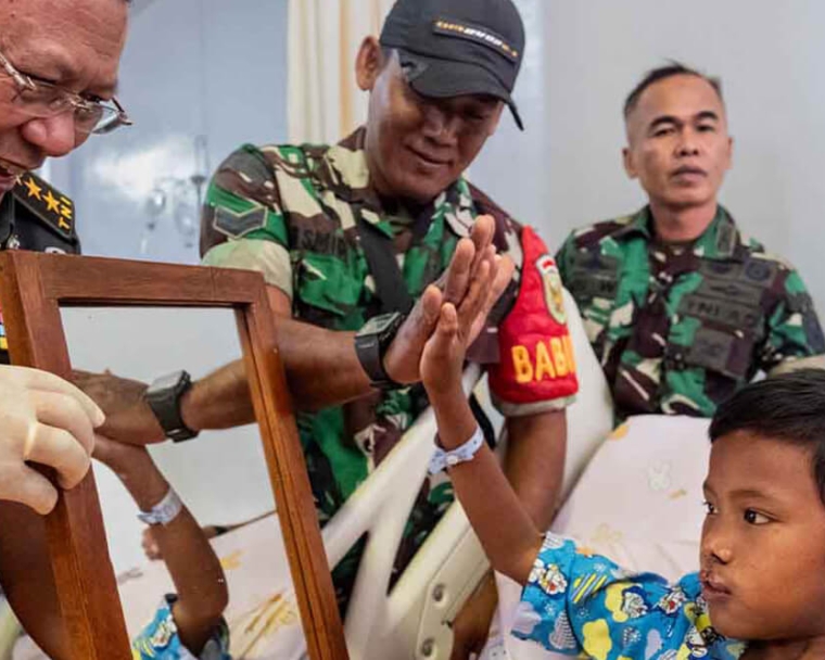 Soldados indonésios sorrindo e cumprimentando Rajib enquanto ele se olha no espelho após a cirurgia de fissura labiopalatina